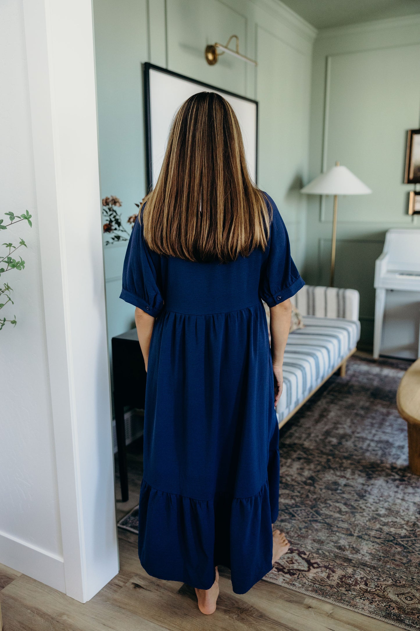 Back view of navy full length dress with short sleeves and ruffle detail on hem.