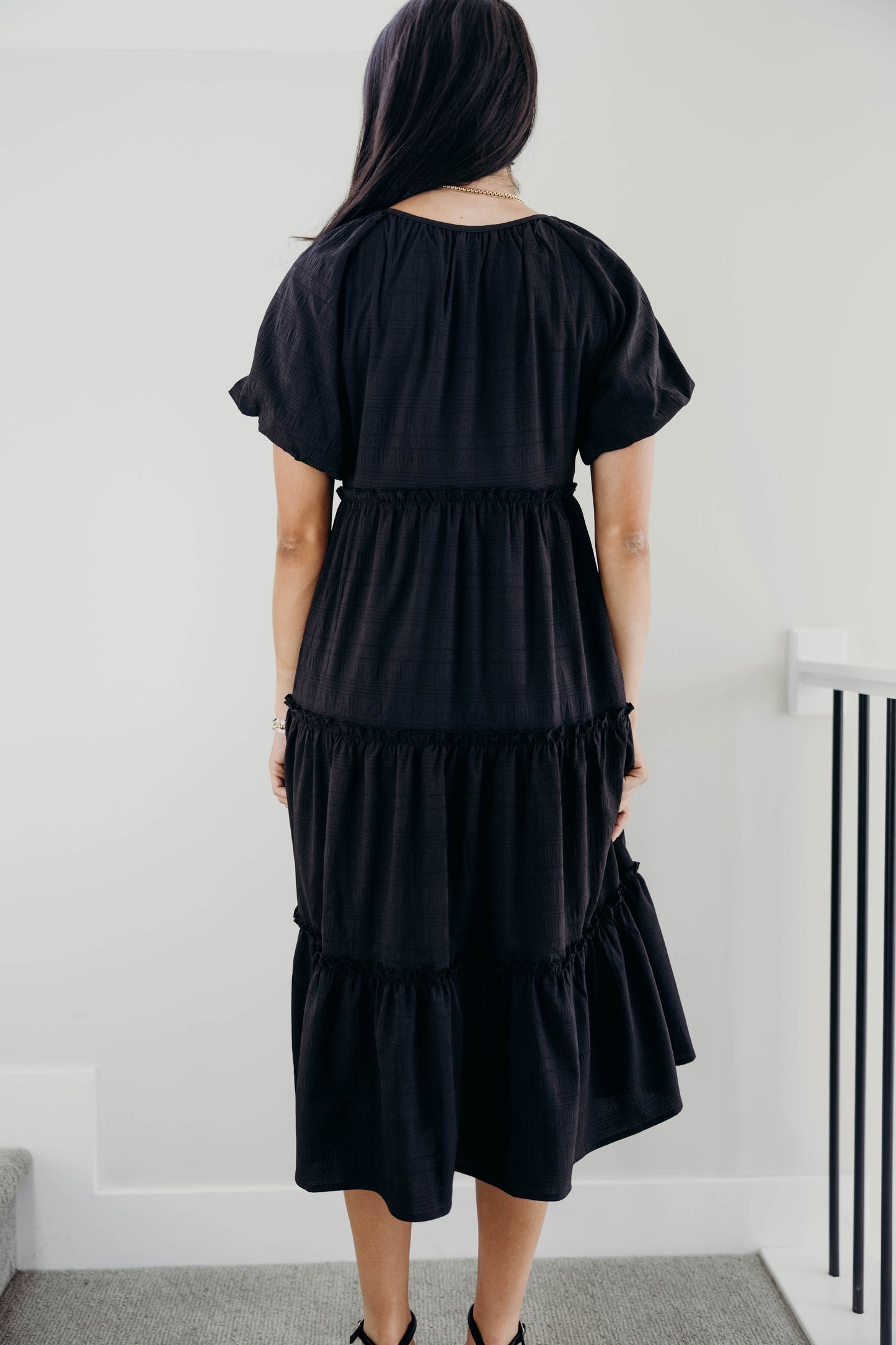 Black textured tiered dress with ruffle detail on tiers, round neckline, and short puff sleeves.