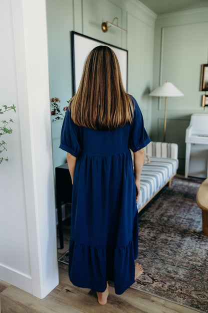 Back view of navy full length dress with short sleeves and ruffle detail on hem.