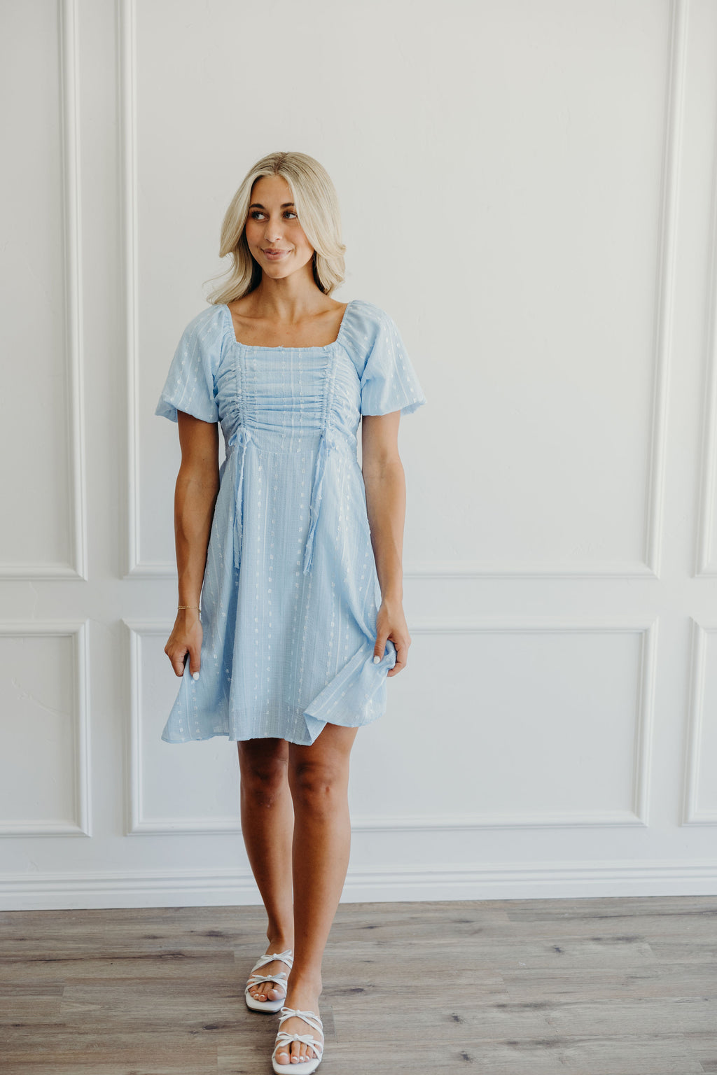 Short blue fit and flare textured dress with gathered and tie detail on bust, square neckline, and short puff sleeves.