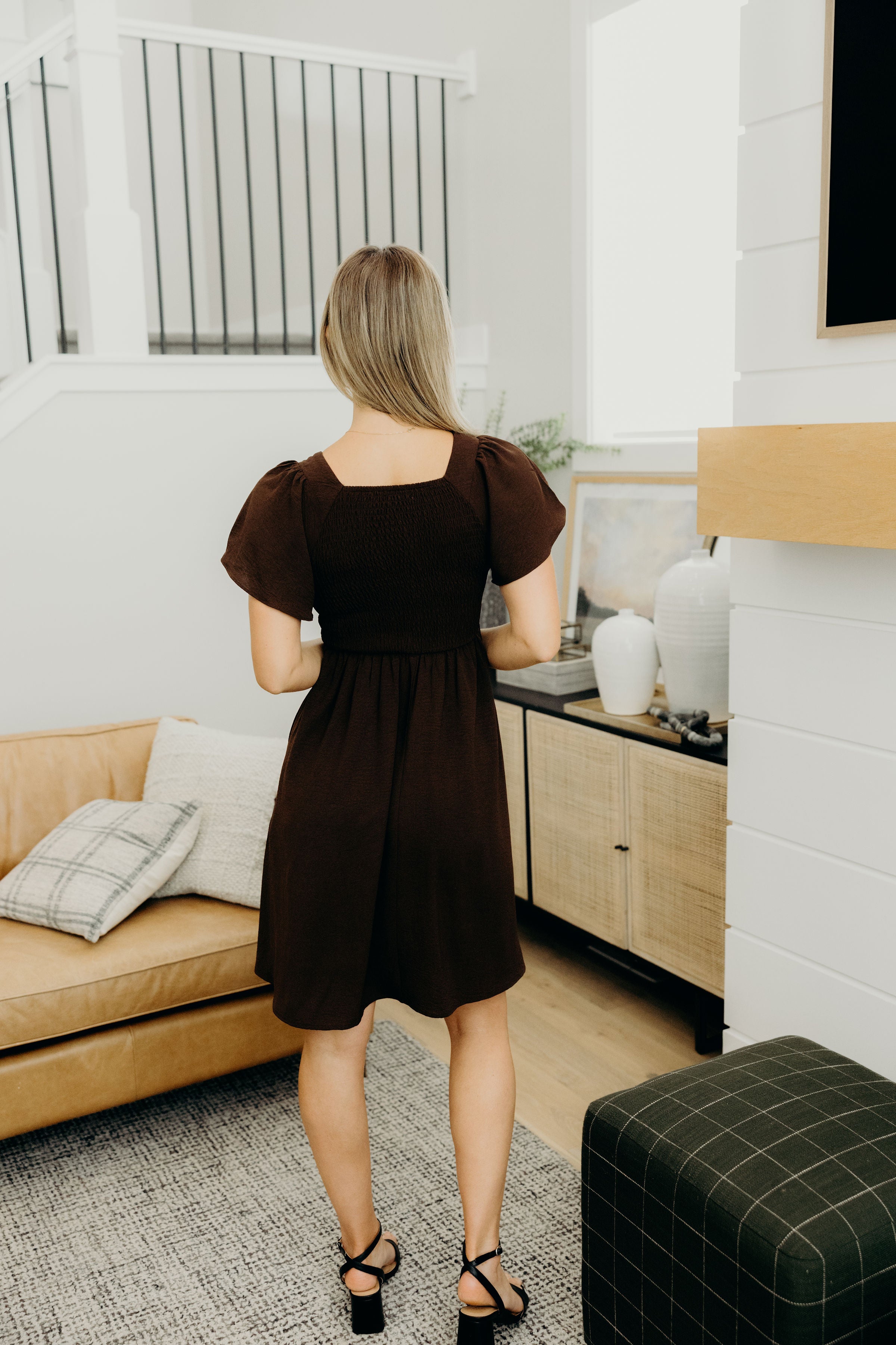 Back view of short fit and flare dress with short flutter sleeves, smocked bodice, and ruffle hem.