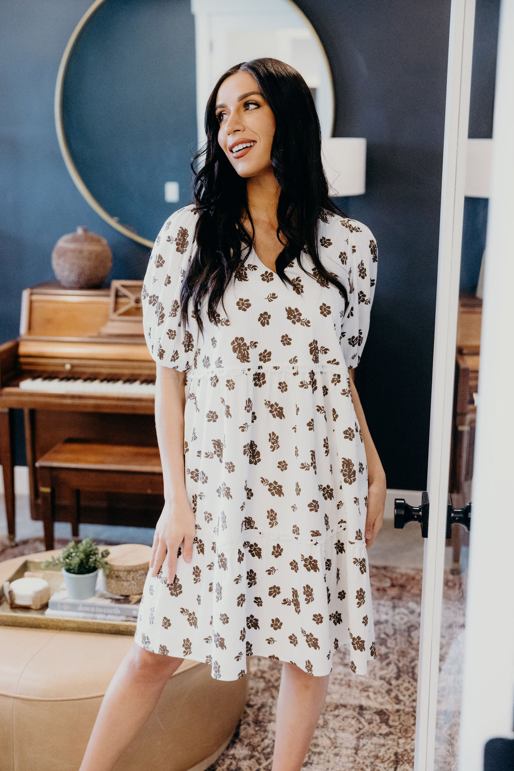 White dress with brown floral print, lace detail at the waist, knee length with puff sleeves.