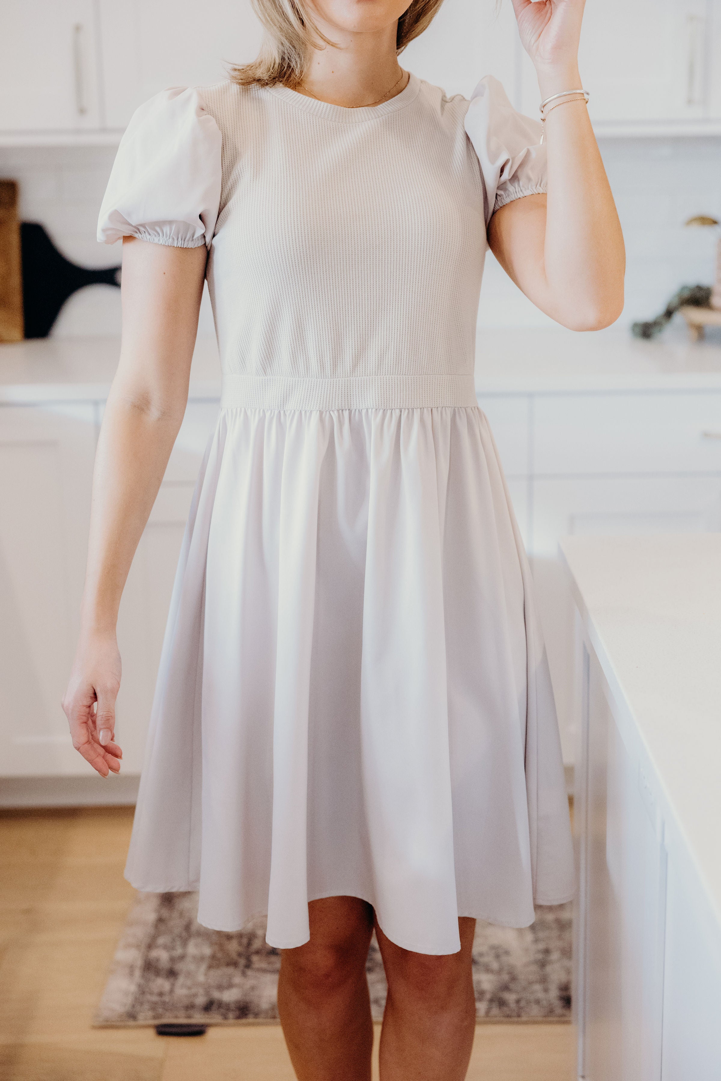 Knee length dress with natural waistline, textured bodice, puff sleeve, and high neckline.