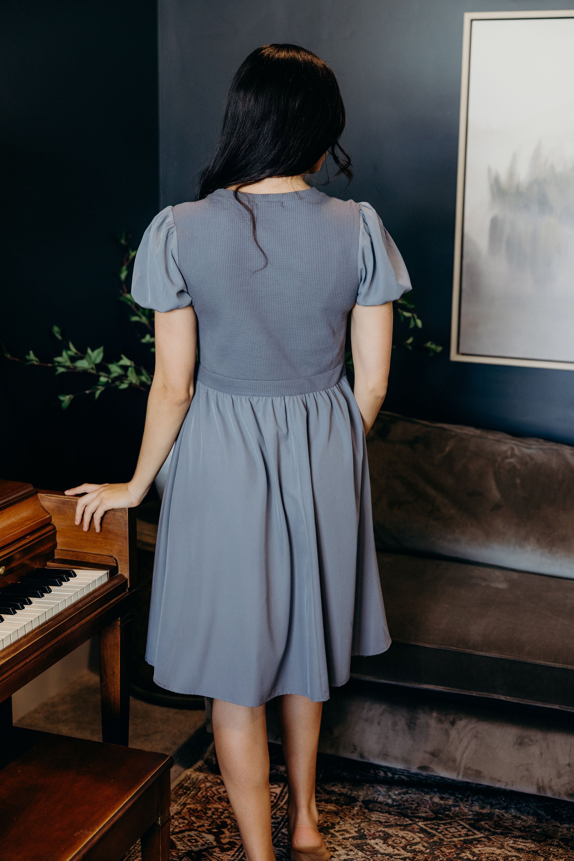 Back view of blue knee length dress with textured bodice and puff sleeves.