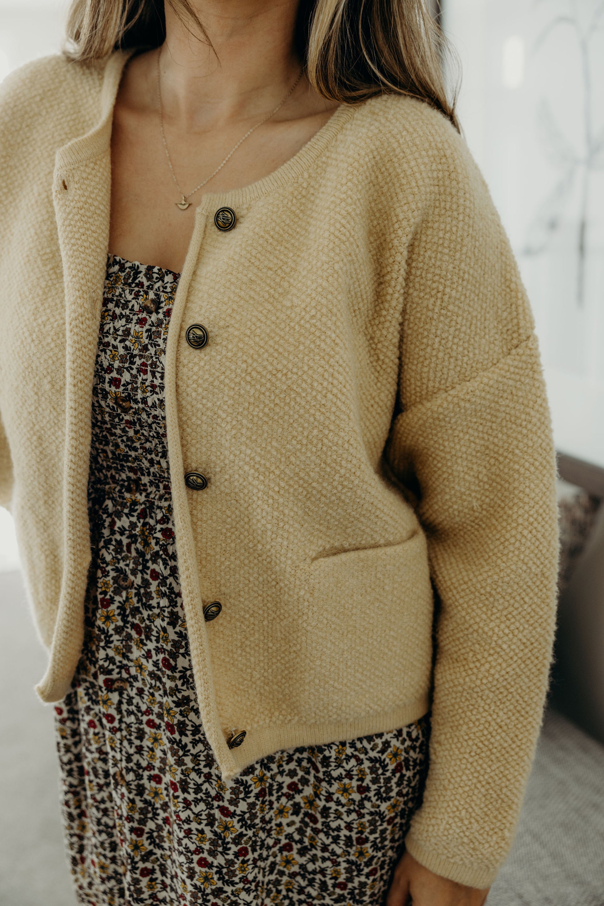Textured knit sweater with front pockets, round neckline, and brass buttons.