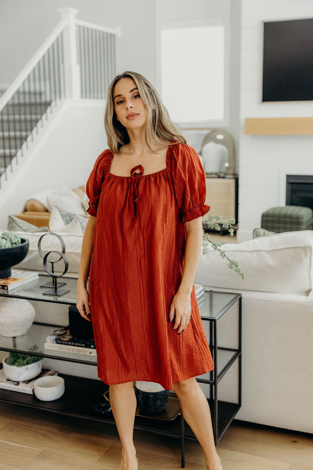 Brick red knee length shift dress with square neckline, and half length puff sleeves with ruffle and tie detail.